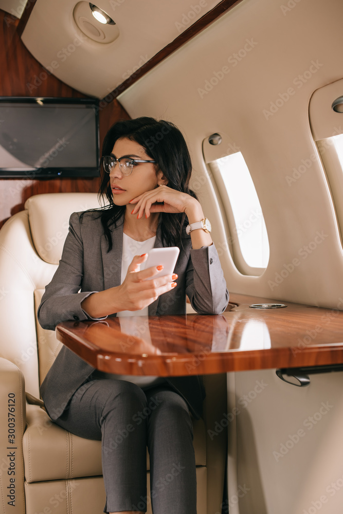 戴眼镜的女商人在私人飞机上使用智能手机的选择性焦点