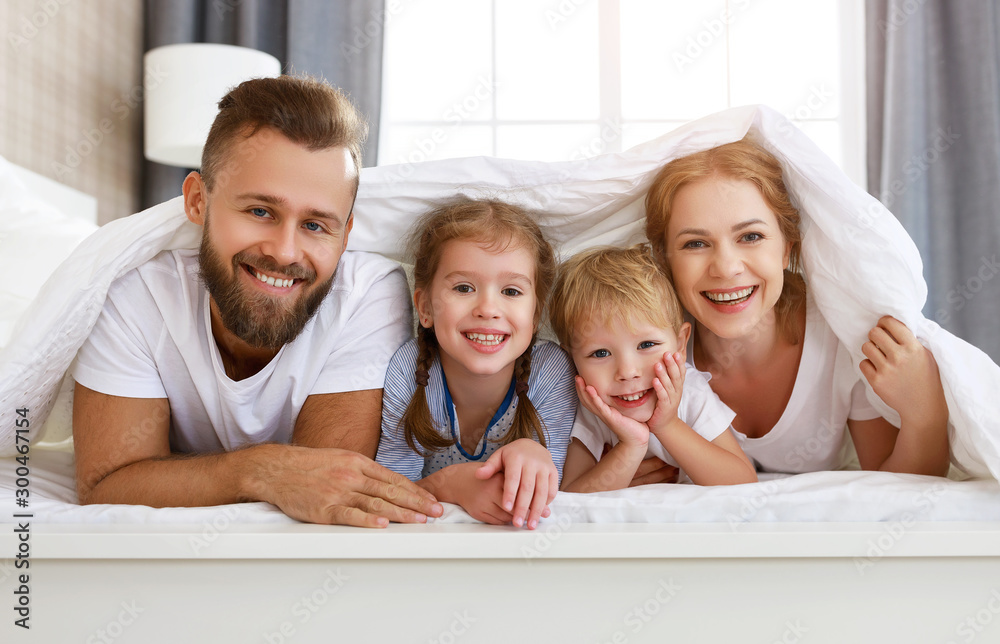 幸福的家庭母亲，父亲和孩子们在家里的床上大笑、玩耍和微笑。