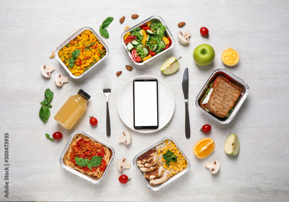 白色木桌上有午餐盒和智能手机的平躺组合，设计模型。健康