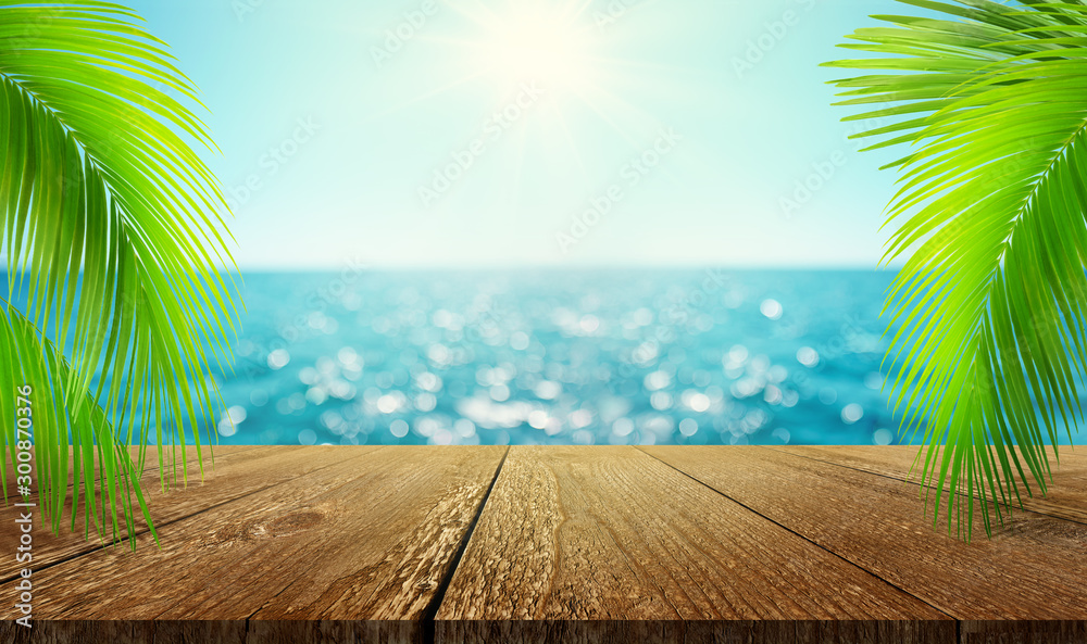 美丽的模糊散焦蓝色海洋背景上有棕榈枝的空木桌模型。总和