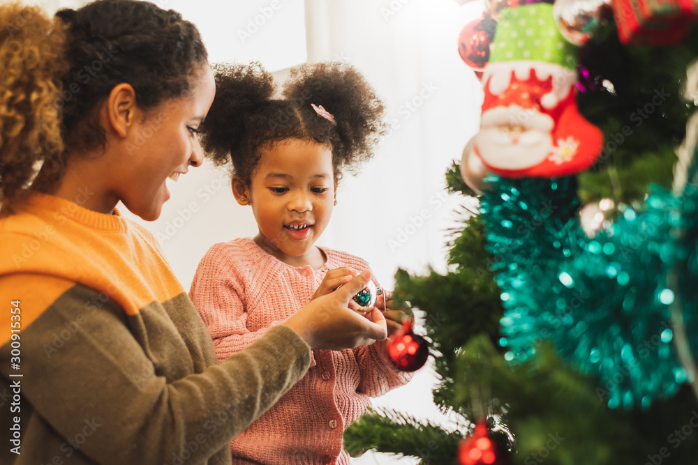 非洲黑人母亲和她可爱的女儿为圣诞节装饰圣诞树，祝你圣诞快乐