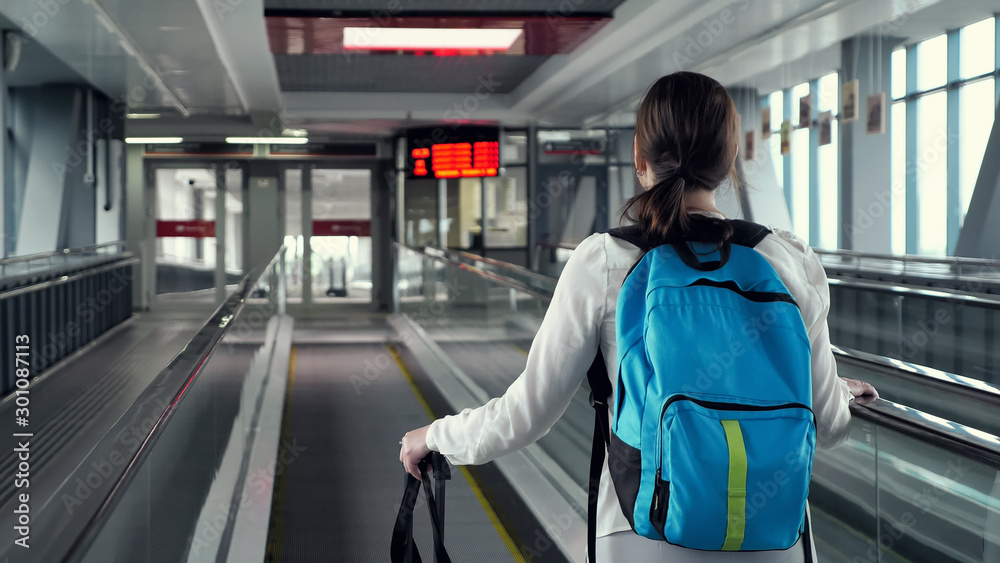 在机场航站楼，背着背包和行李箱坐在自动扶梯上的年轻女子。她要去t