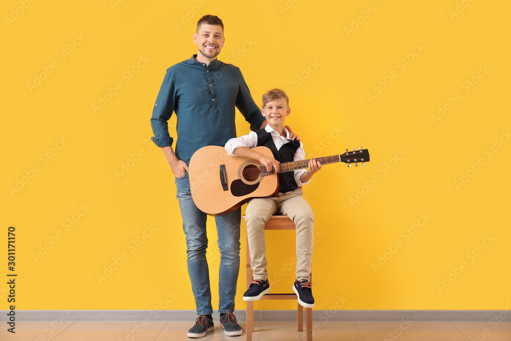 英俊的男人和他的小儿子在彩色墙附近拿着吉他