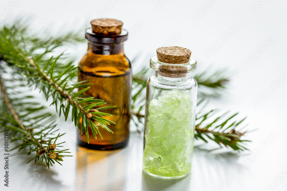 白色桌子背景上有毛皮树枝的瓶子里的化妆品云杉油和盐