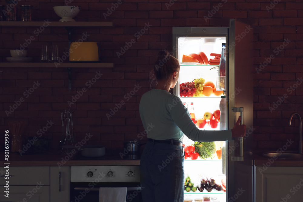 Young woman choosing food in refrigerator at night