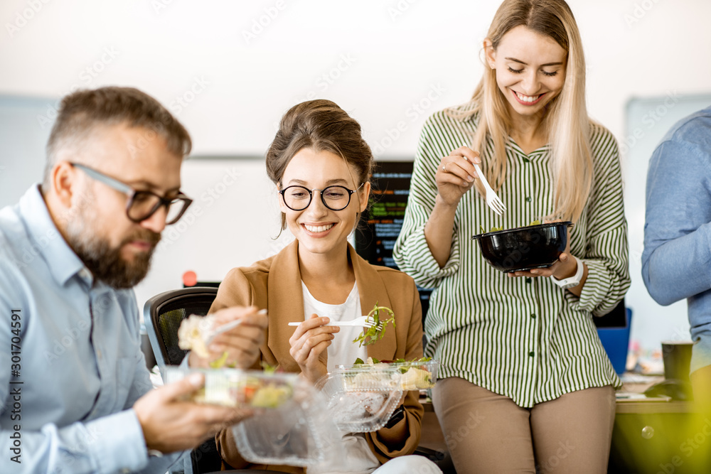 Group of diverse colleagues eating takeaway salad, sitting together and having fun during a lunchtim