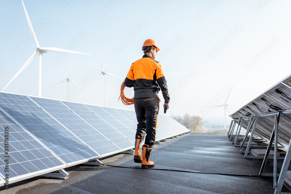 穿着橙色防护服的设备精良的工人在光电伏特上行走和检查太阳能电池板