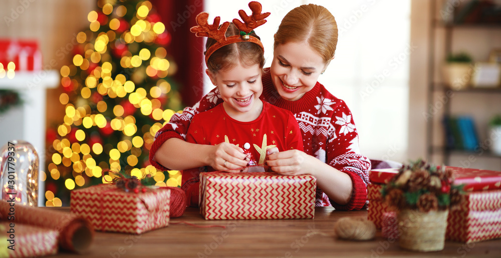 幸福家庭母子在圣诞树附近的家里打包圣诞礼物