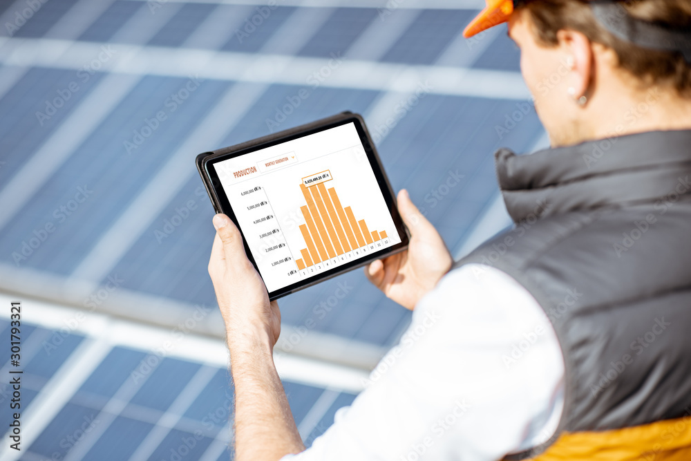 Man examining genaration of solar power plant, holding digital tablet with a chart of electricity pr