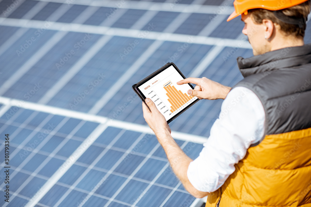 一名男子正在检查太阳能发电厂的发电量，手里拿着一块有电力图表的数字平板电脑