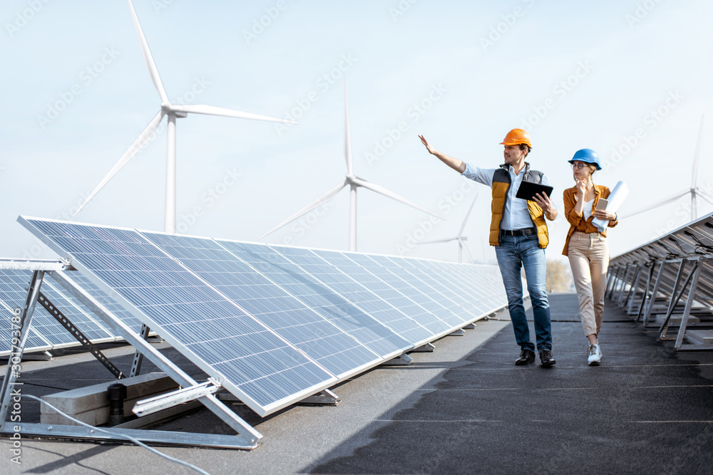 屋顶太阳能发电厂的视图，两名工程师正在散步并检查光伏电池板。