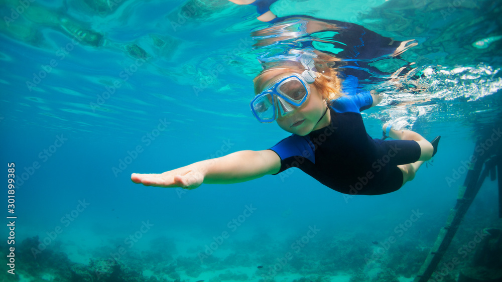 戴着浮潜面罩和潜水服的快乐小孩在珊瑚礁泻湖的水下跳跃和潜水。F