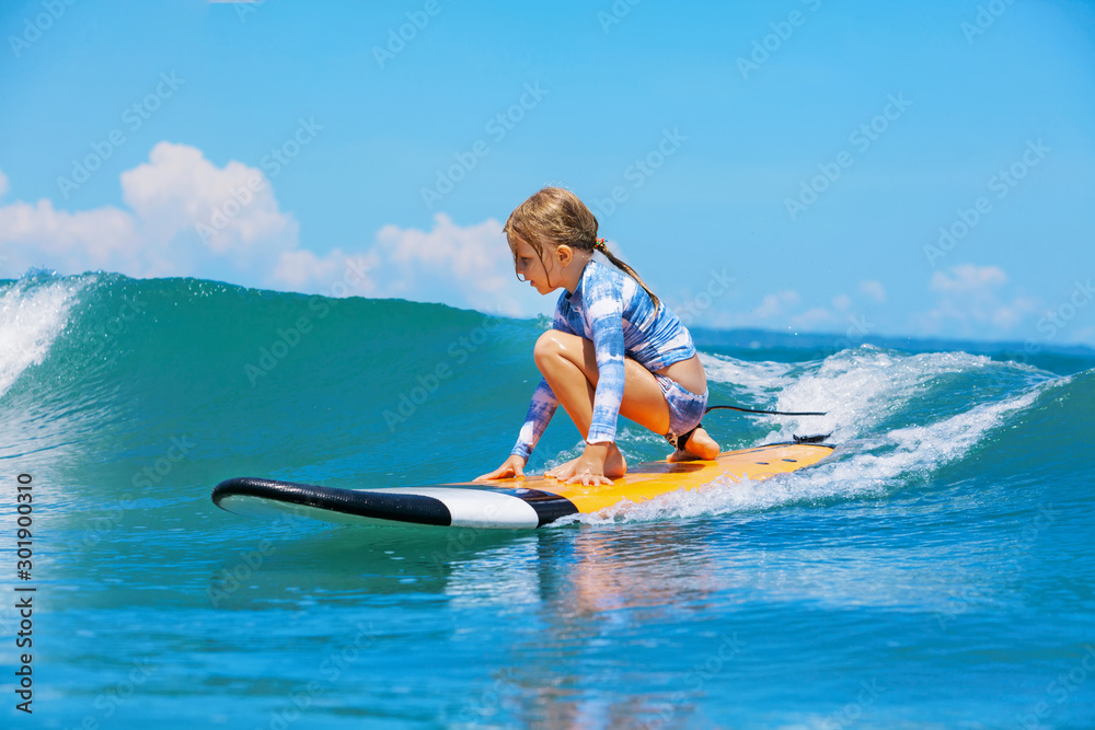 Happy baby girl - young surfer ride on surfboard with fun on sea waves. Active family lifestyle, kid