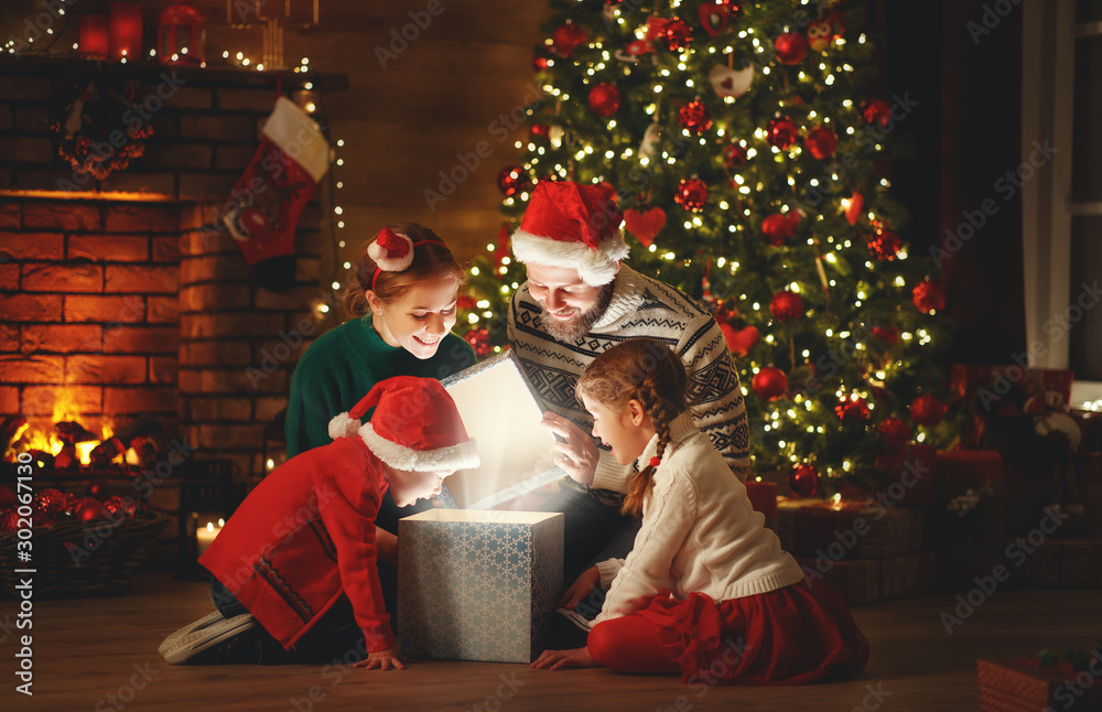 圣诞快乐！快乐的家庭母亲、父亲和孩子们在家里的树旁送上了魔法礼物。
