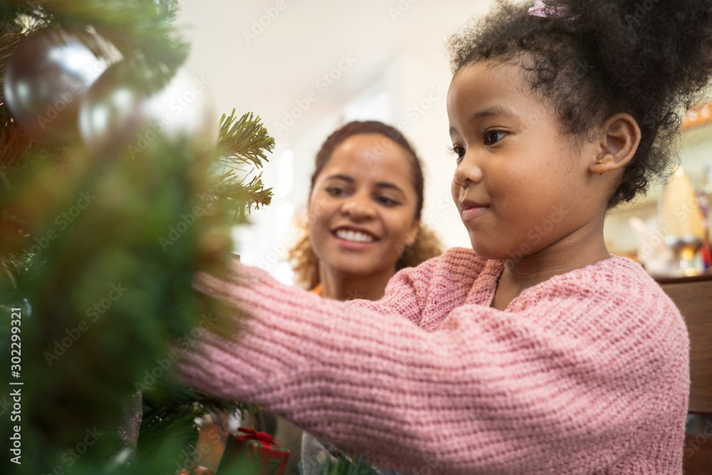 Mother and daughter african american girl decorating Christmas tree with ,arranging the christmas li