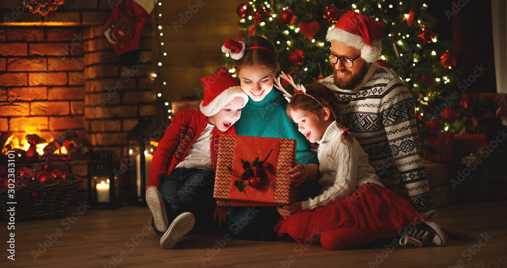 圣诞快乐！快乐的家庭母亲、父亲和孩子们在家里的树旁送上了魔法礼物。