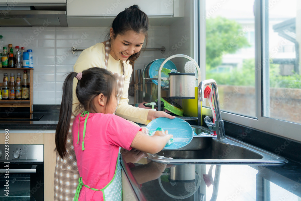 美丽的亚洲母女在水槽上与洗涤剂一起洗碗，玩得很开心