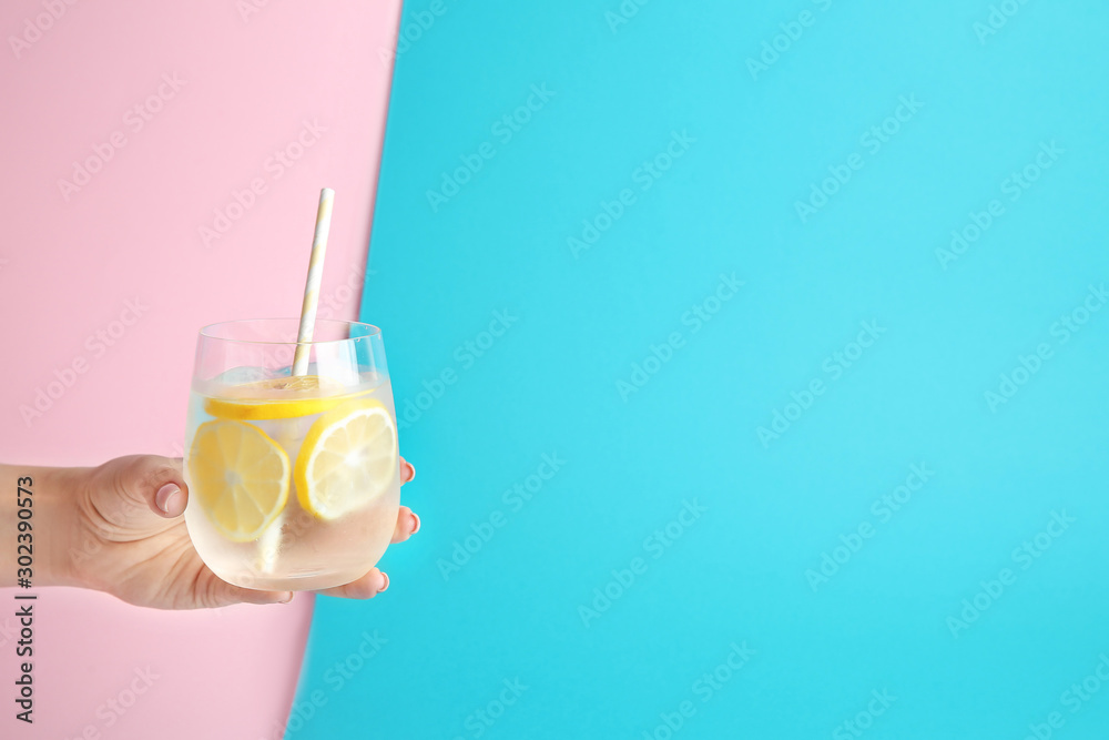 彩色背景上有一杯新鲜柠檬水的女性手