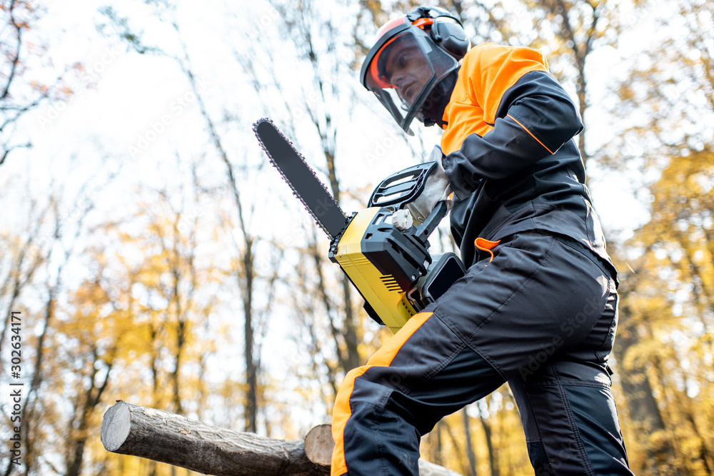穿着防护服的专业伐木工人在森林里用链锯工作。伐木工人马克