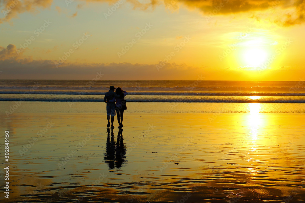 sunset with the silhouette of romantic couple with  reflection  on the beach in bali -indonesia