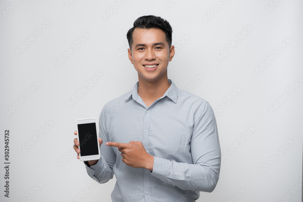 快乐快乐的亚洲年轻人拿着智能手机指着手机屏幕，展示了令人敬畏的新产品
