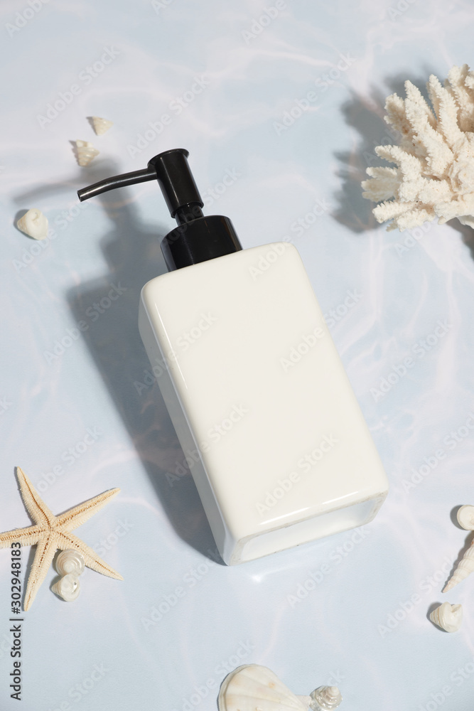 White cosmetic product/ shampoo bottle sea shells on light pastel blue background.