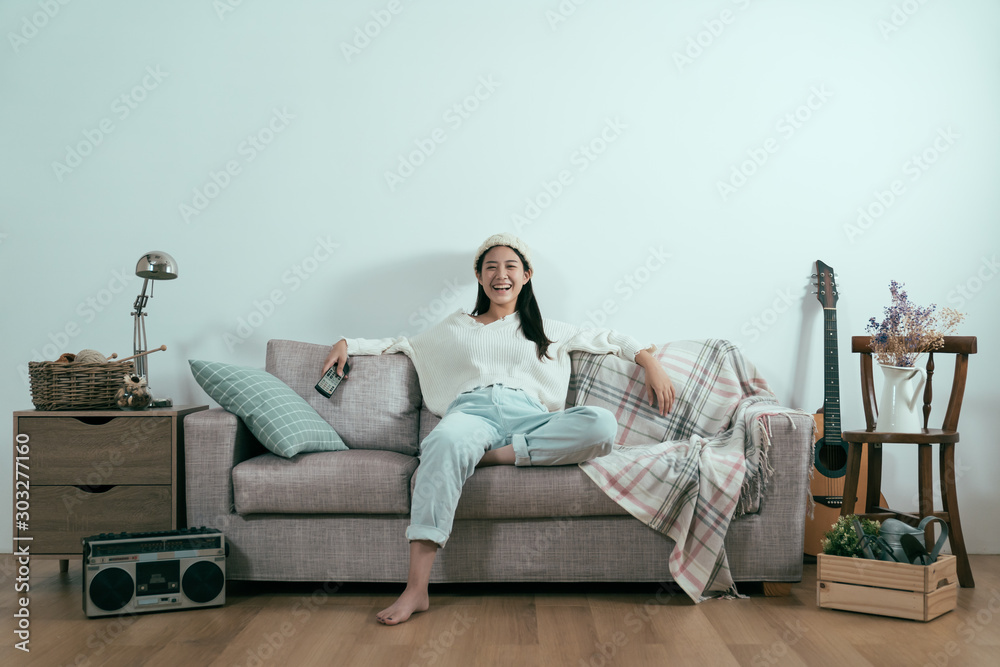 carefree asian woman watching TV at home sitting on sofa in modern winter apartment. Young laughing 