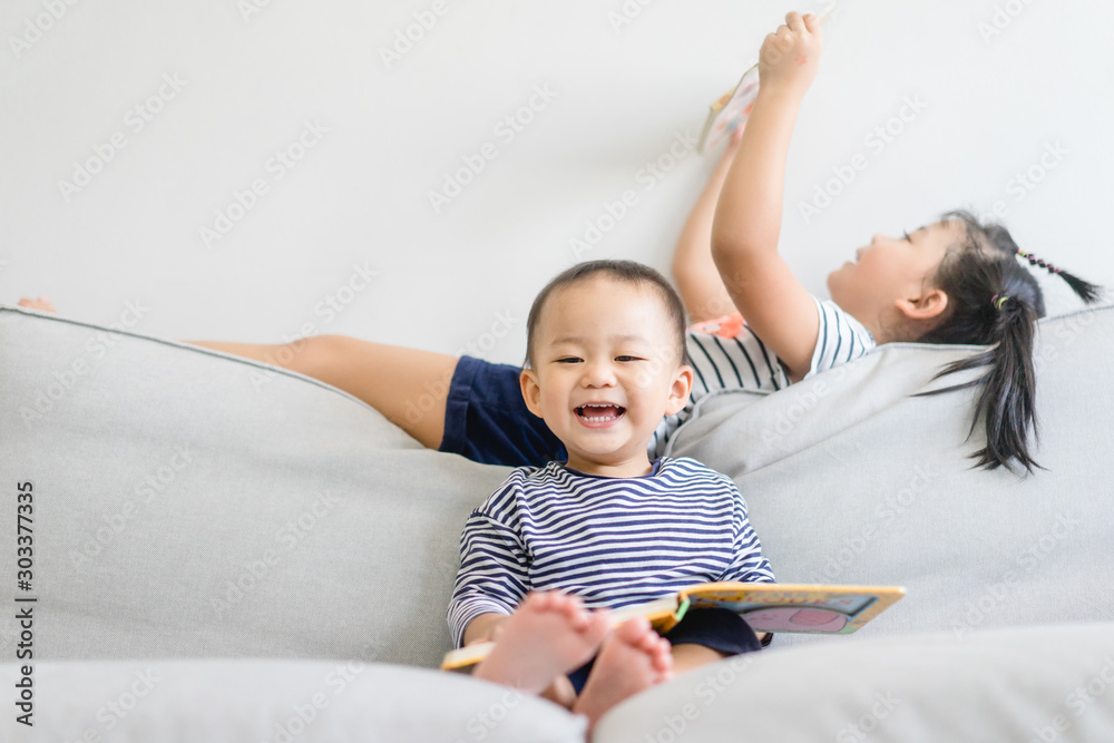 小妹妹和她的小弟弟在沙发床上读故事。可爱的女孩和小男孩在家放松