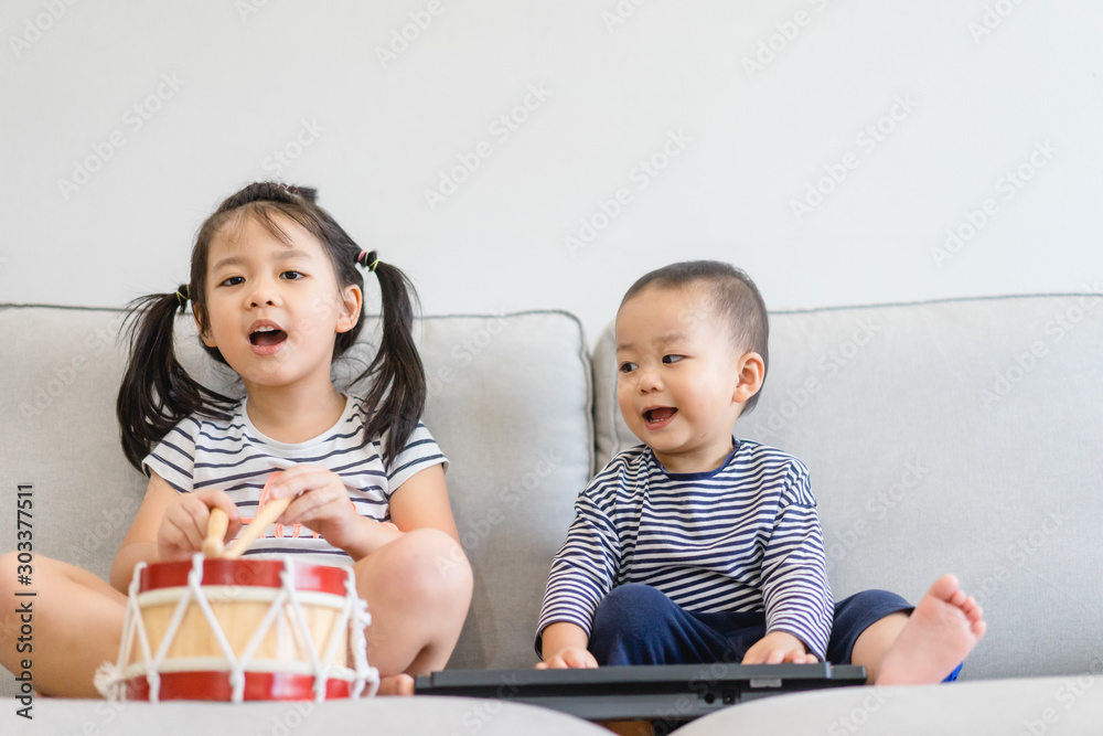 小妹妹和她的小弟弟玩键盘、鼓和唱歌。亚洲孩子玩和唱歌