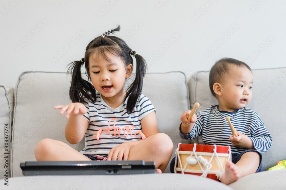 小妹妹和她的小弟弟玩键盘、鼓和唱歌。亚洲孩子玩和唱歌