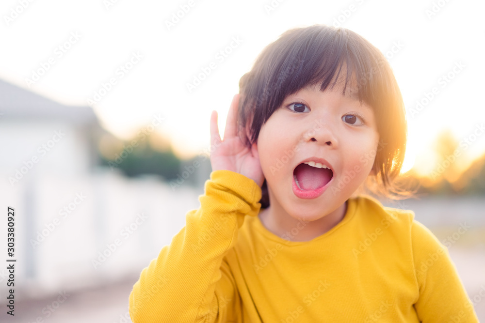 亚洲小女孩把手放在耳朵附近，听着什么。有趣的孩子g激动人心的表情
