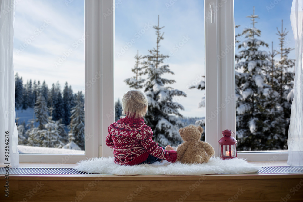 可爱的金发孩子，男孩，拿着泰迪熊朋友玩具坐在窗帘上，看着风景