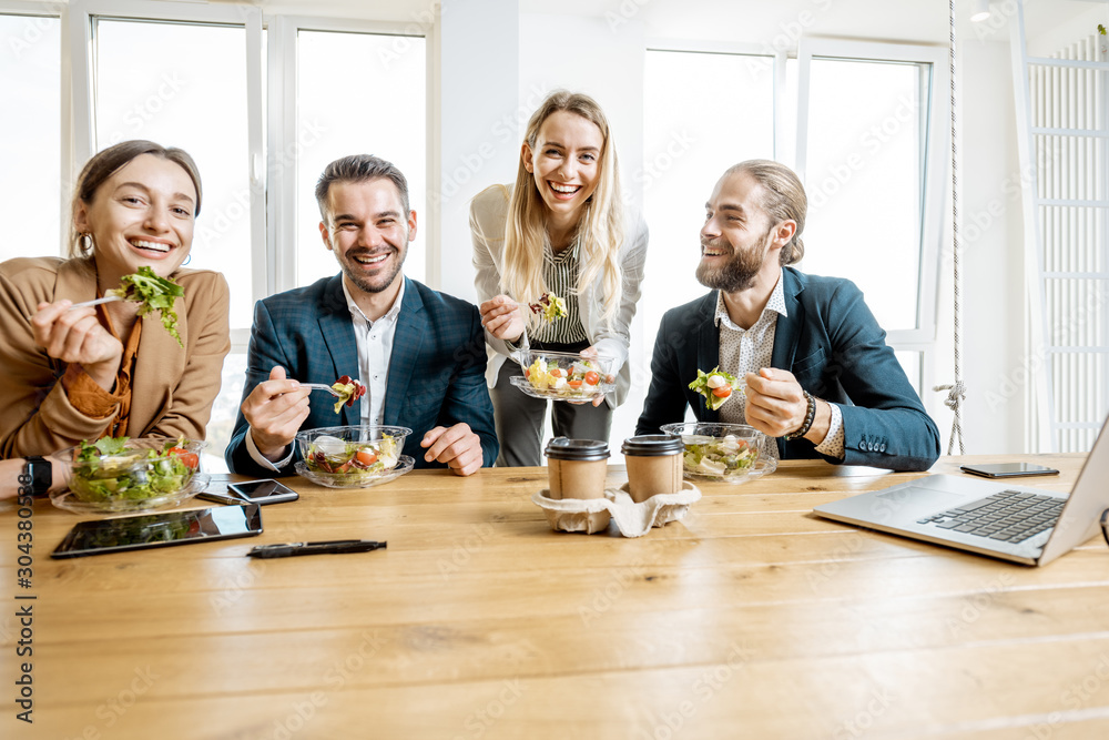Group of a young office workers eating salads and drinking coffee at the modern office canteen. Conc