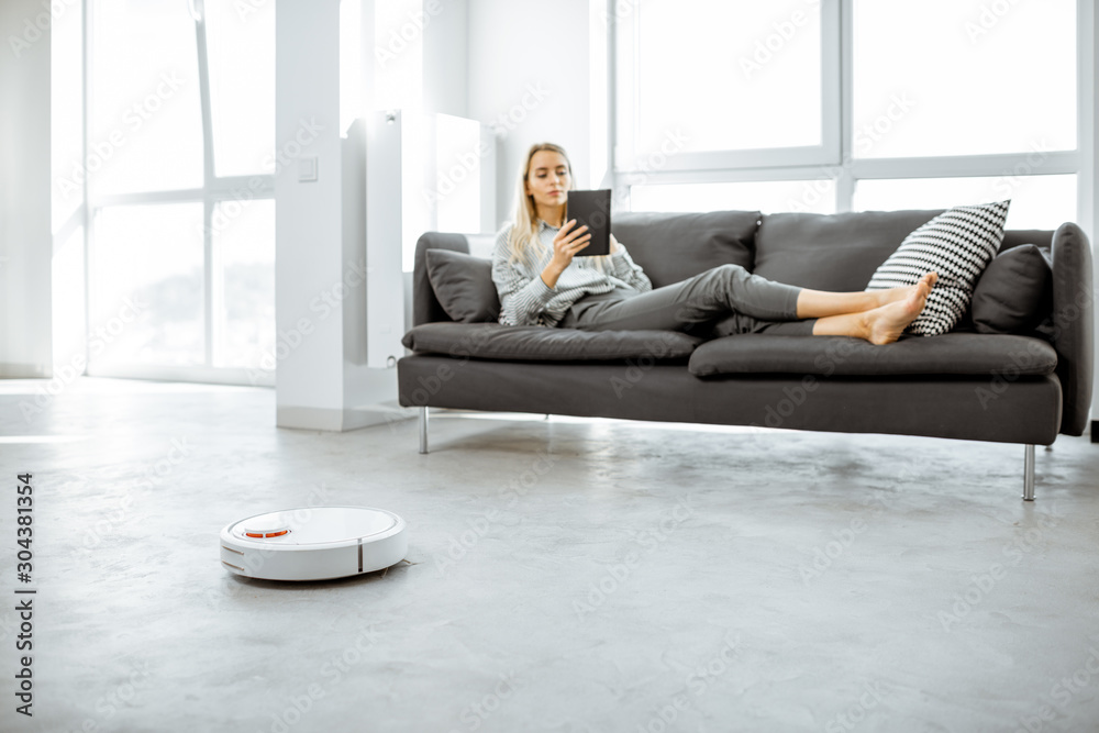 女人在沙发上放松，自动吸尘器穿着现代白色l做家务