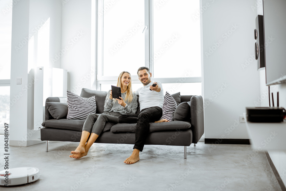 Young couple relaxing on the comfortable couch, watching television in the bright living room of the