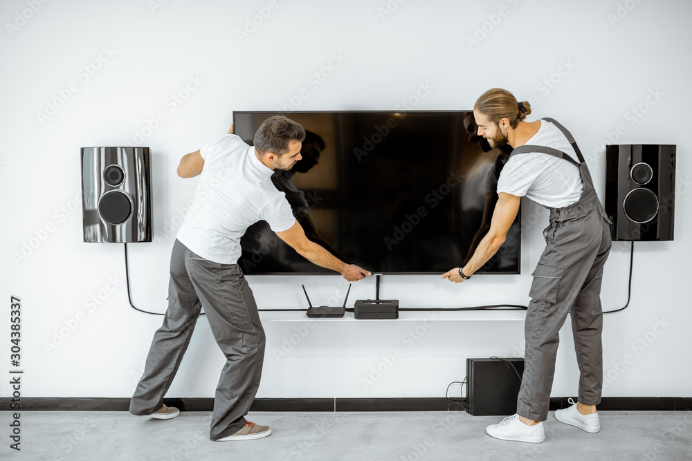 两名穿着工作服的专业工人在白色liv中安装大型电视监视器和音频系统