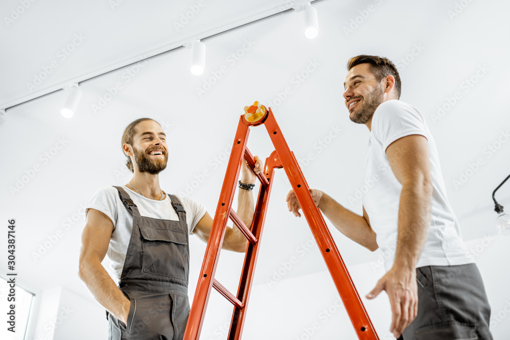 两个穿着制服的英俊工人在家里修理时在梯子上交谈