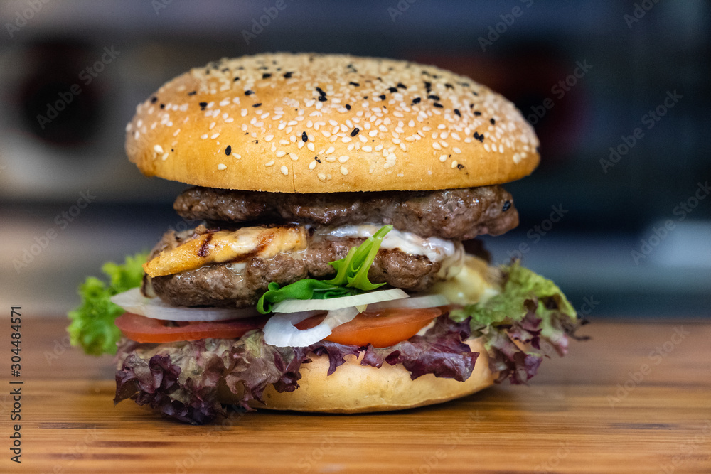 一个新鲜的彩色大汉堡，在木托盘上放肉、蛋、沙拉、洋葱圈和蘸酱