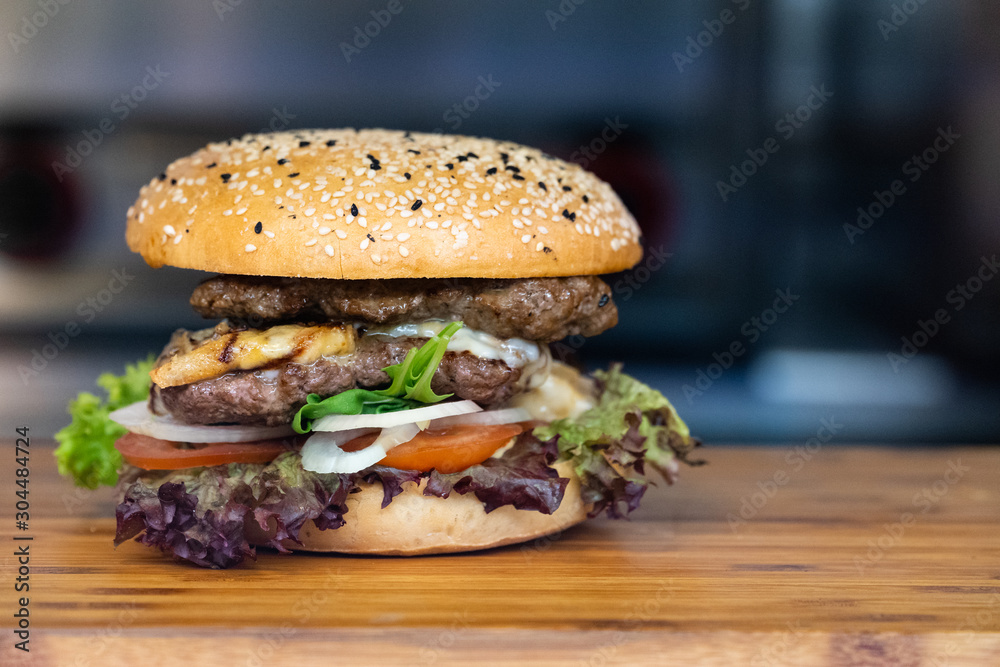 一个新鲜多彩的大汉堡，里面有肉、蛋、沙拉、洋葱圈和蘸酱，放在木托盘上
