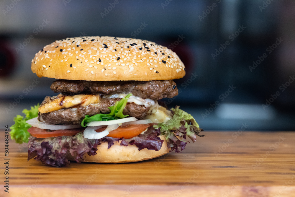 一个新鲜的彩色大汉堡，在木托盘上放肉、蛋、沙拉、洋葱圈和蘸酱