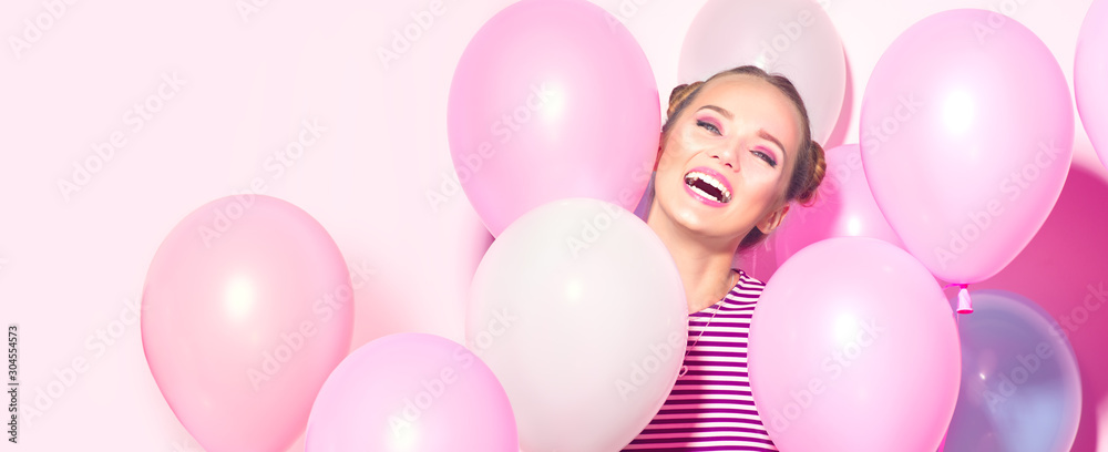 美丽的女孩，带着五颜六色的气球，在粉红色的背景下大笑。美丽快乐的年轻女人