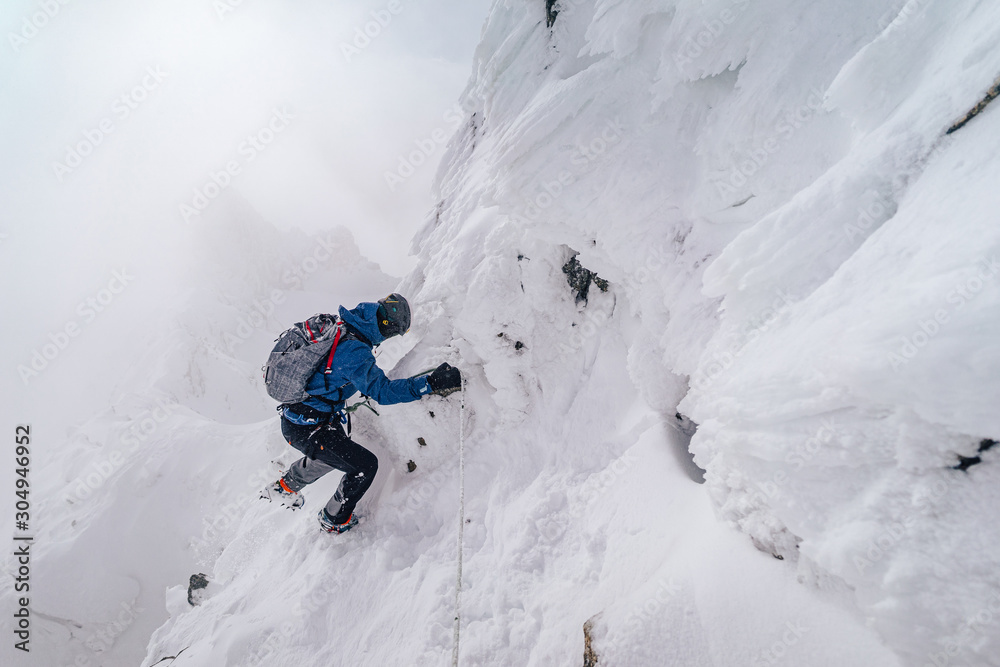An alpinist climbing an alpine ridge in winter extreme conditions. Adventure ascent of alpine peak i