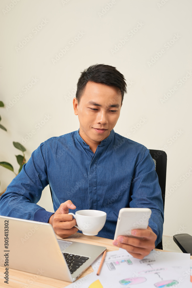 商人在工作场所喝茶/咖啡时使用手机的肖像