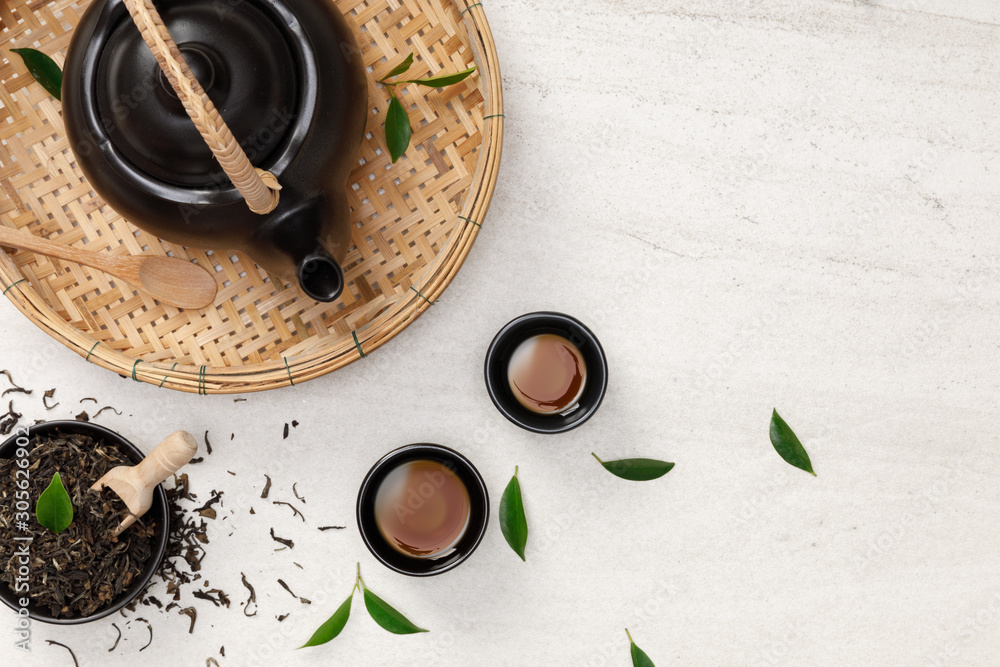 白石桌上的一杯热茶，配茶壶、绿茶叶和干香草俯视图