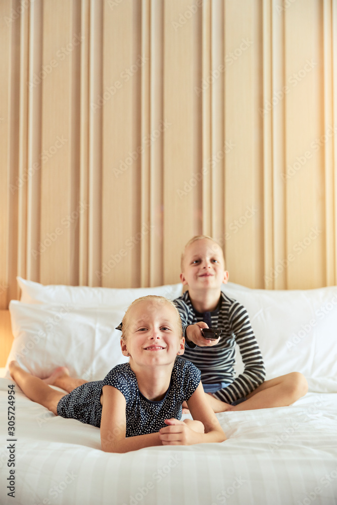 Smiling girl and her brother watching television on a bed