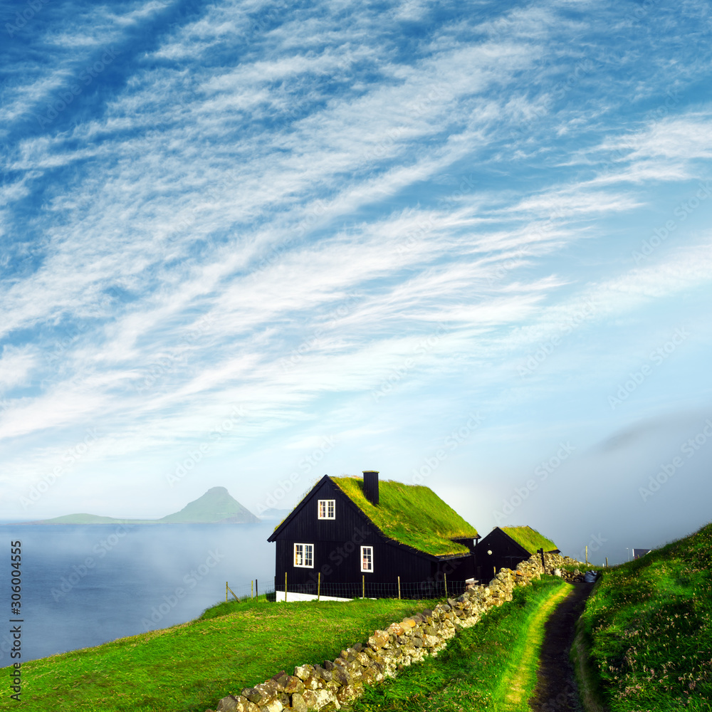 在Velbastadu，一栋典型的草坪顶草屋顶和蓝色多云天空的房子的雾蒙蒙的晨景