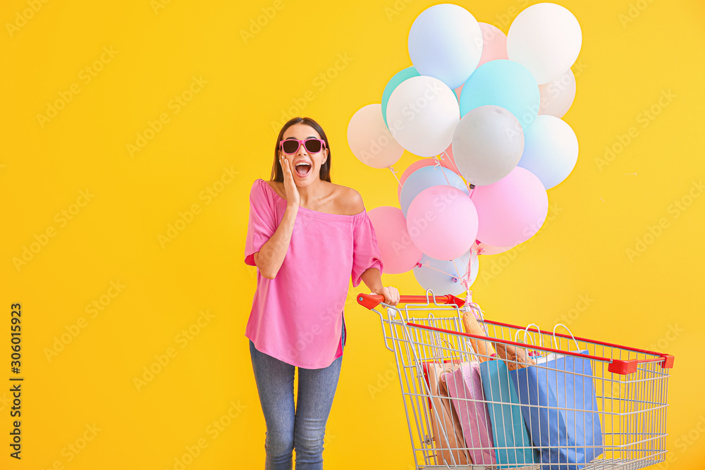 带着购物车和彩色背景气球的惊喜年轻女子