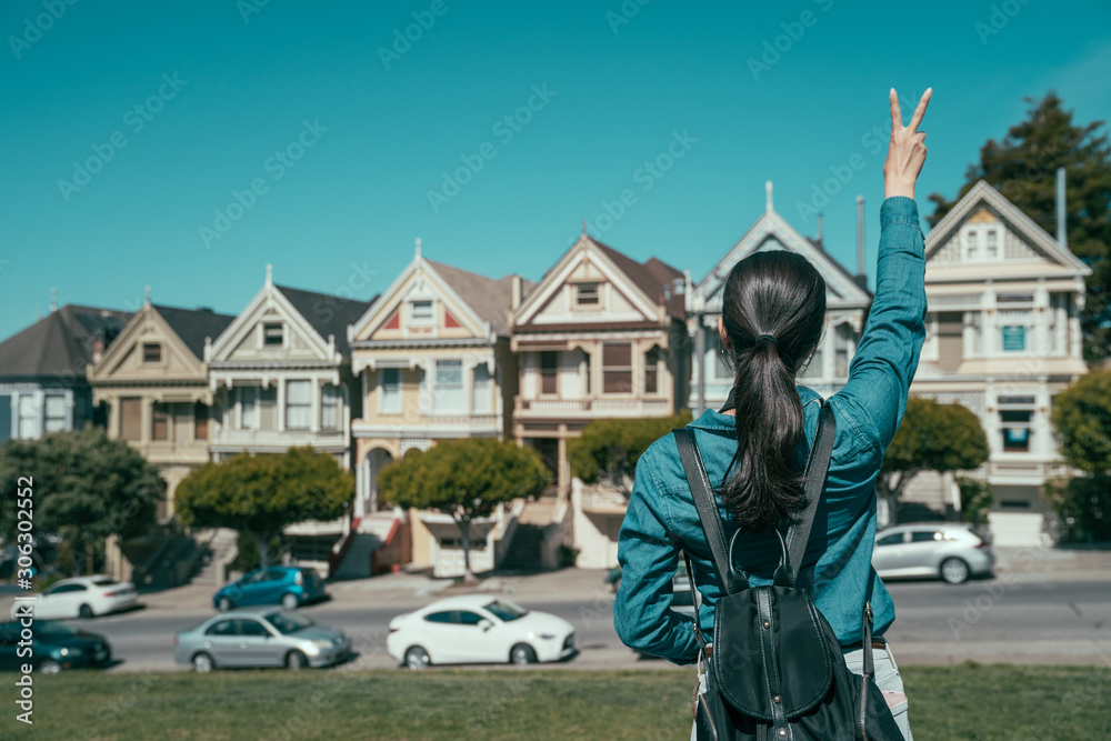 back view portrait of young girl with backpack showing v sign while raising hands. female tourist si