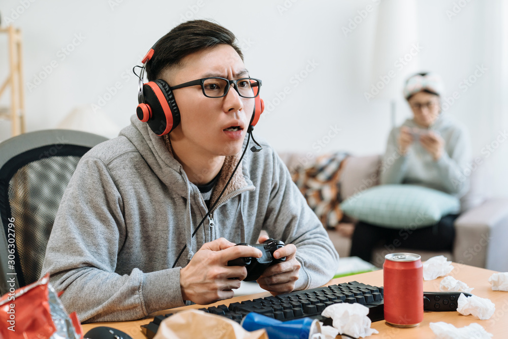 boyfriend playing online video games at home in living room. young guy in glasses and headphone sitt