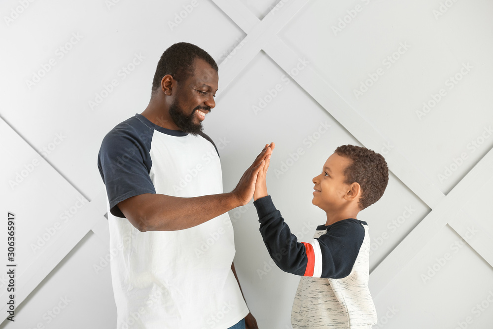非裔美国人和他的小儿子在浅色背景下互相击掌的肖像